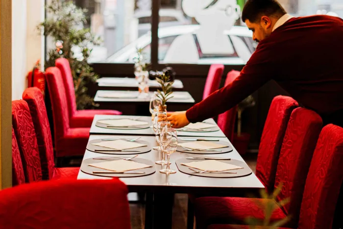 Membre de l'équipe dressant une grande table près de la vitrine du restaurant, verres alignés avant le service