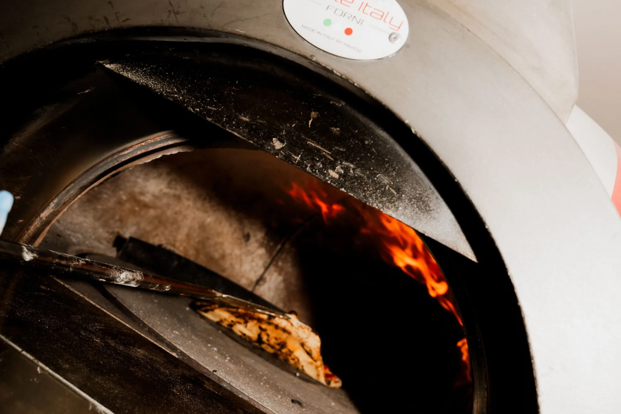 Pizza en cuisson au centre d'un four à bois, pâte dorée éclairée par les flammes orangées