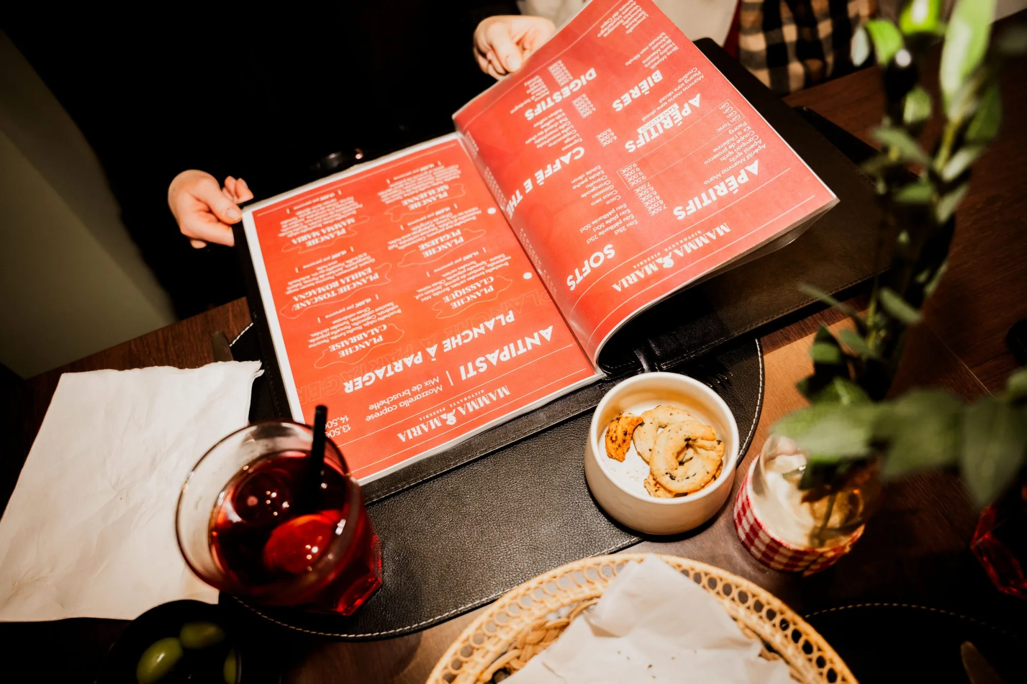 La carte rouge de Mamma Maria ouverte sur la table, avec un verre de vin et un antipasto posés à côté