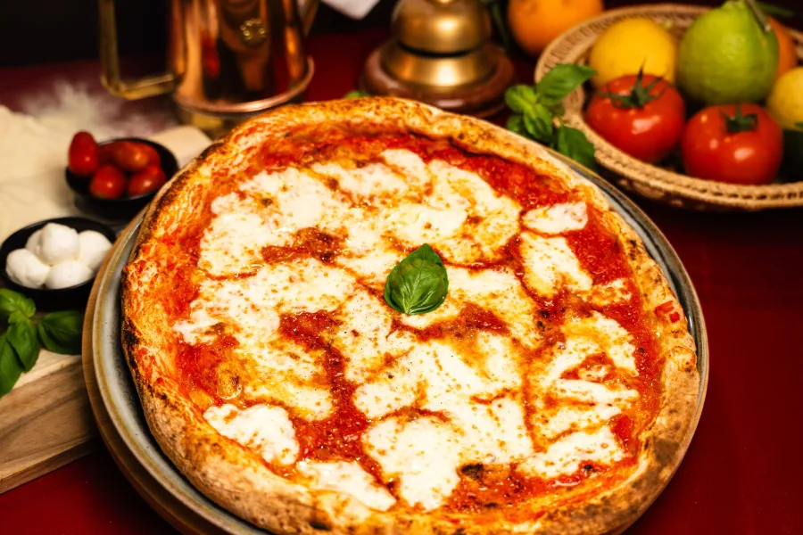 Pizza margherita posée sur une assiette en métal, une feuille de basilic déposée au centre du fromage fondu