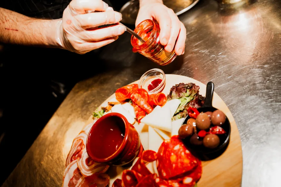 Plateau d'antipasti garni de jambon, fromage, olives et poivrons grillés, avec une sauce versée dessus à table
