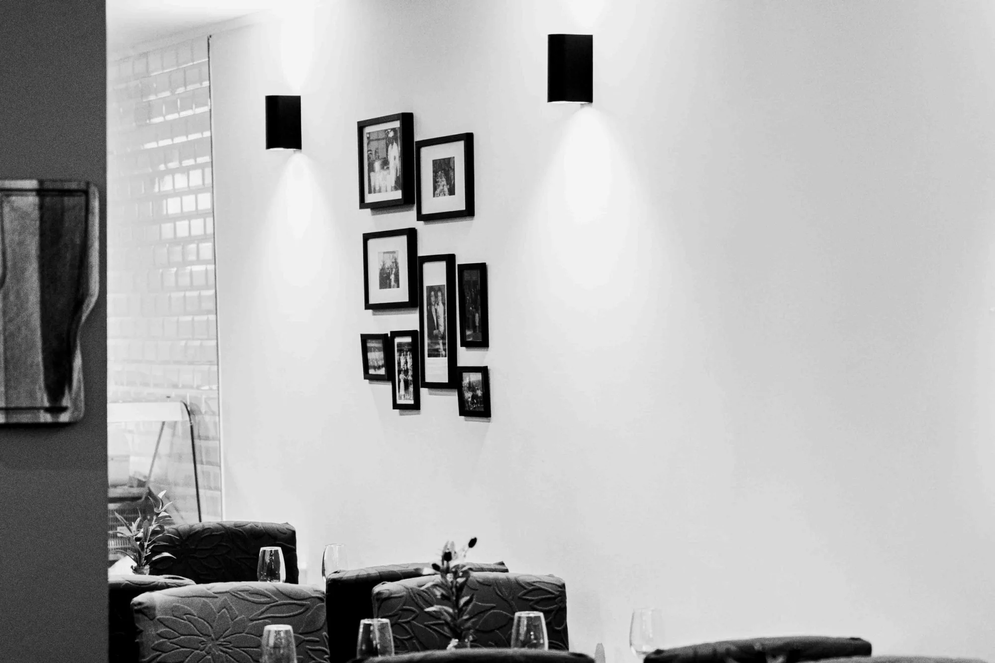 Mur blanc orné de photographies encadrées en noir et blanc, tables dressées disposées juste devant dans la salle