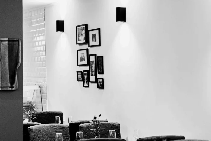 Mur blanc orné de photographies encadrées en noir et blanc, tables dressées disposées juste devant dans la salle