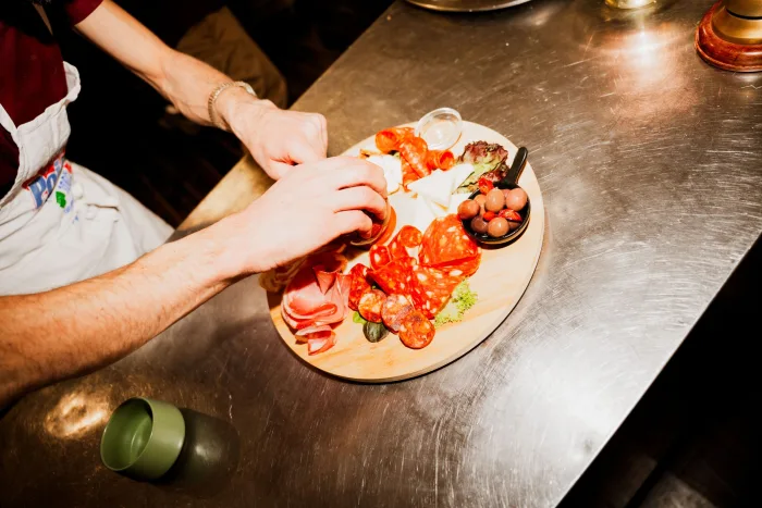 Planche de charcuterie et légumes grillés dressée sur le plan de travail inox de la cuisine